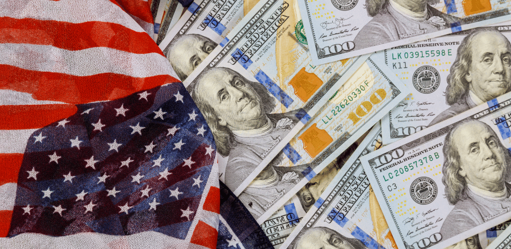 A pile of U.S. hundred-dollar bills partially covered by an American flag.